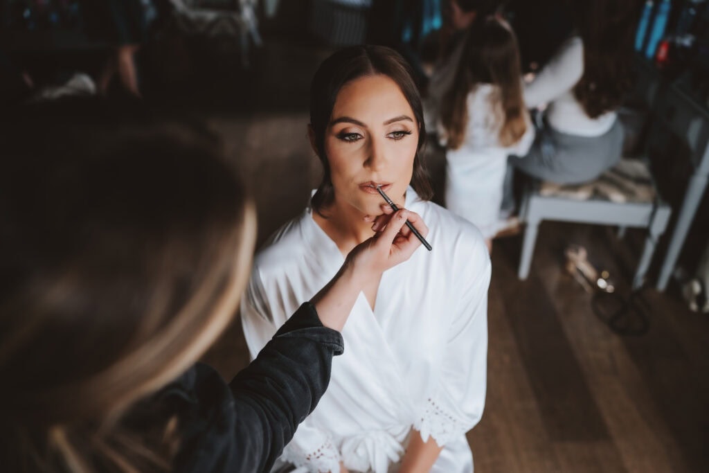 Rebecca having her makeup applied on her wedding morning in the Granary at Crondon Park, Essex — bridal preparations photographed by Tel, Lily & White