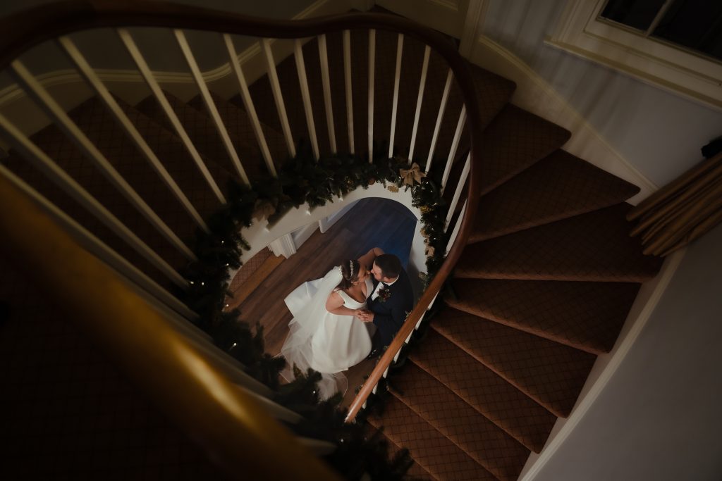 Overhead view of bride and groom on the staircase at Fennes wedding venue in Essex — creative architectural wedding photography by Lily & White