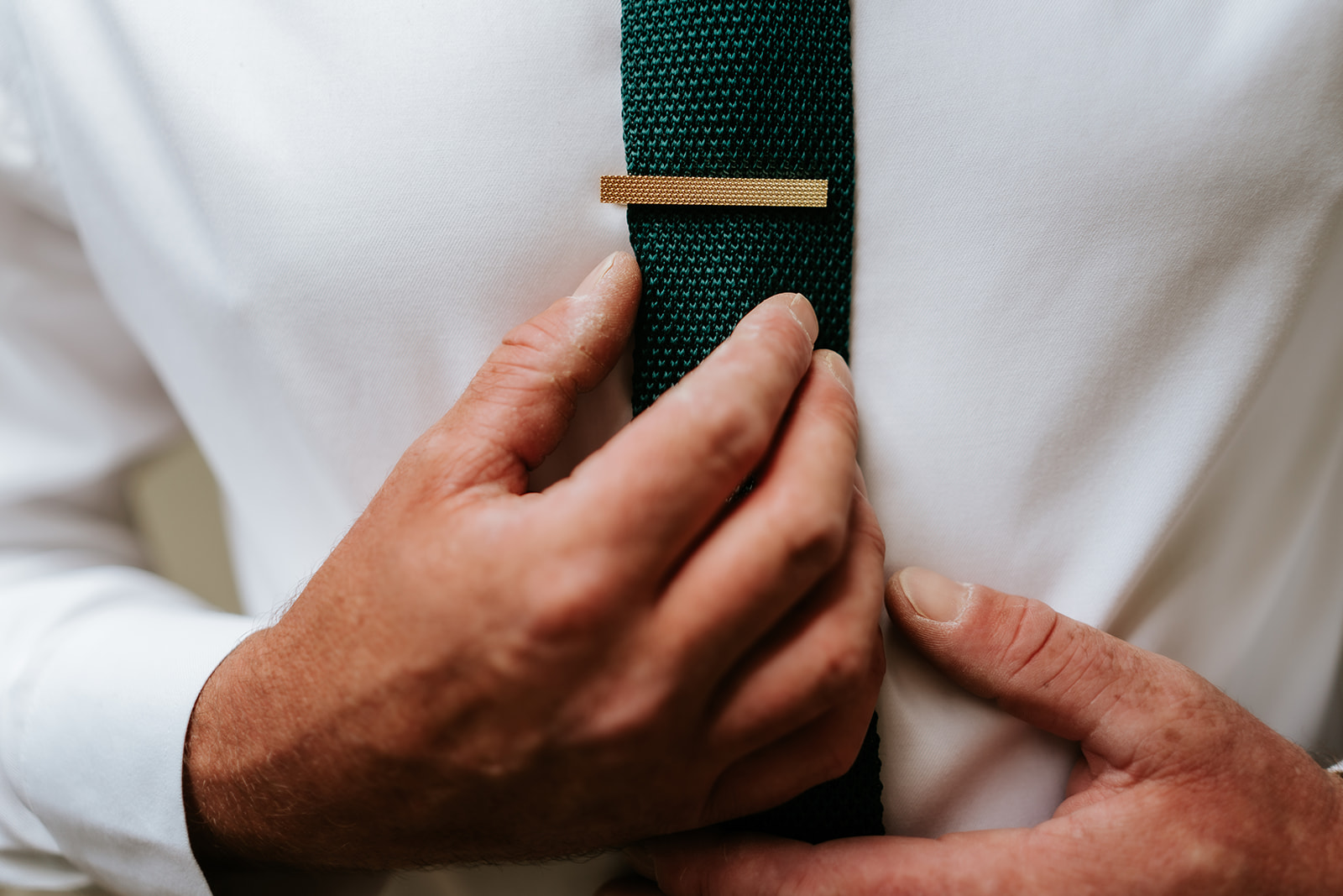 A candid photograph of a groom adjusting his tie before his wedding.