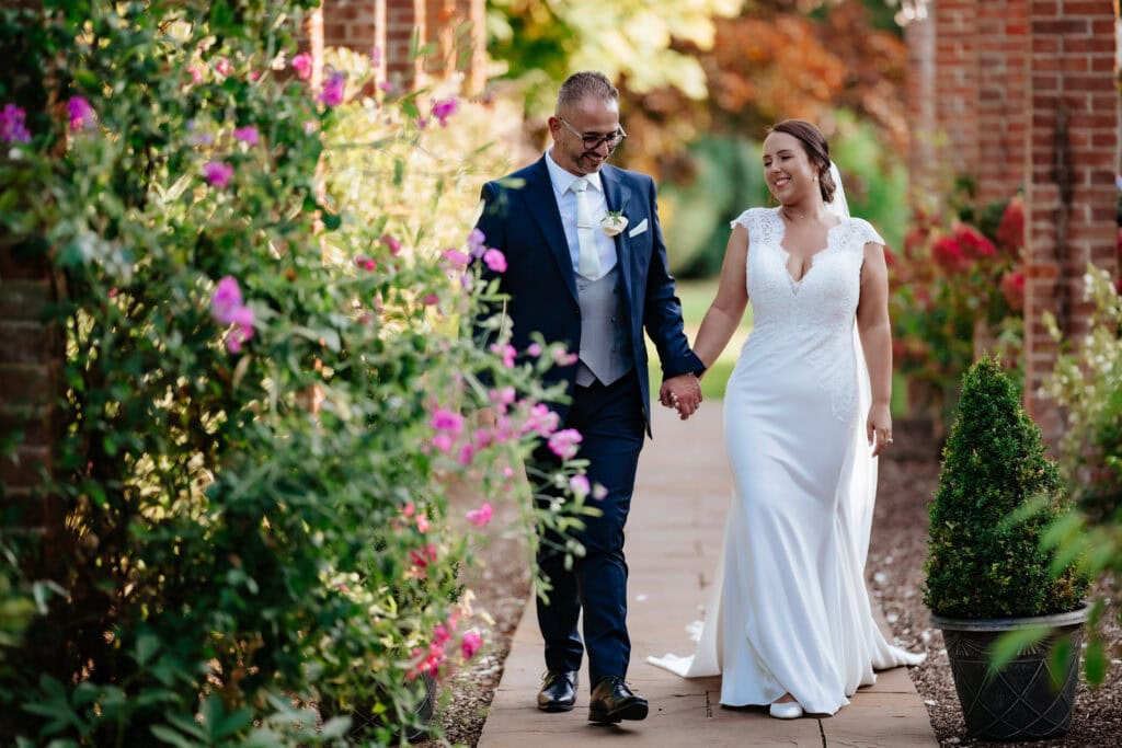 Steph and Oz walking hand in hand through the walled garden at Hutton Hall, Brentwood, Essex, late summer flowers in full colour behind them – 2nd September 2023, photographed by Tel, Lily & White