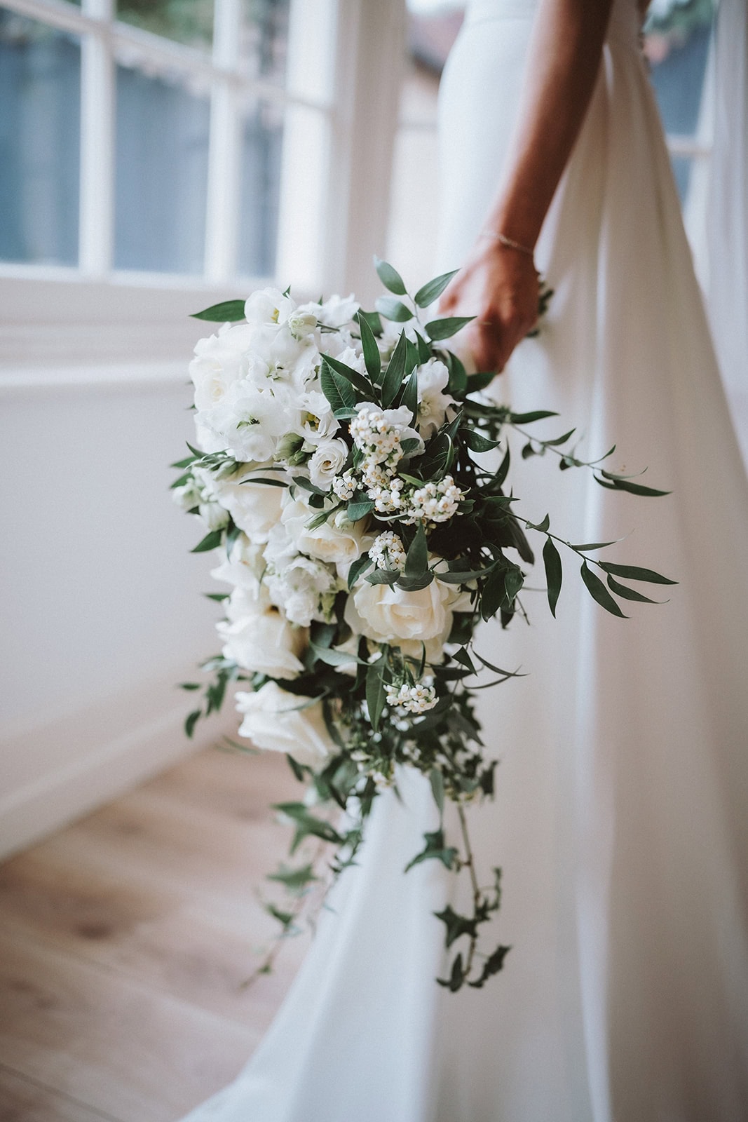 Editorial wedding photographer Essex; close-up detail of a bride holding a lush white and green floral bouquet.