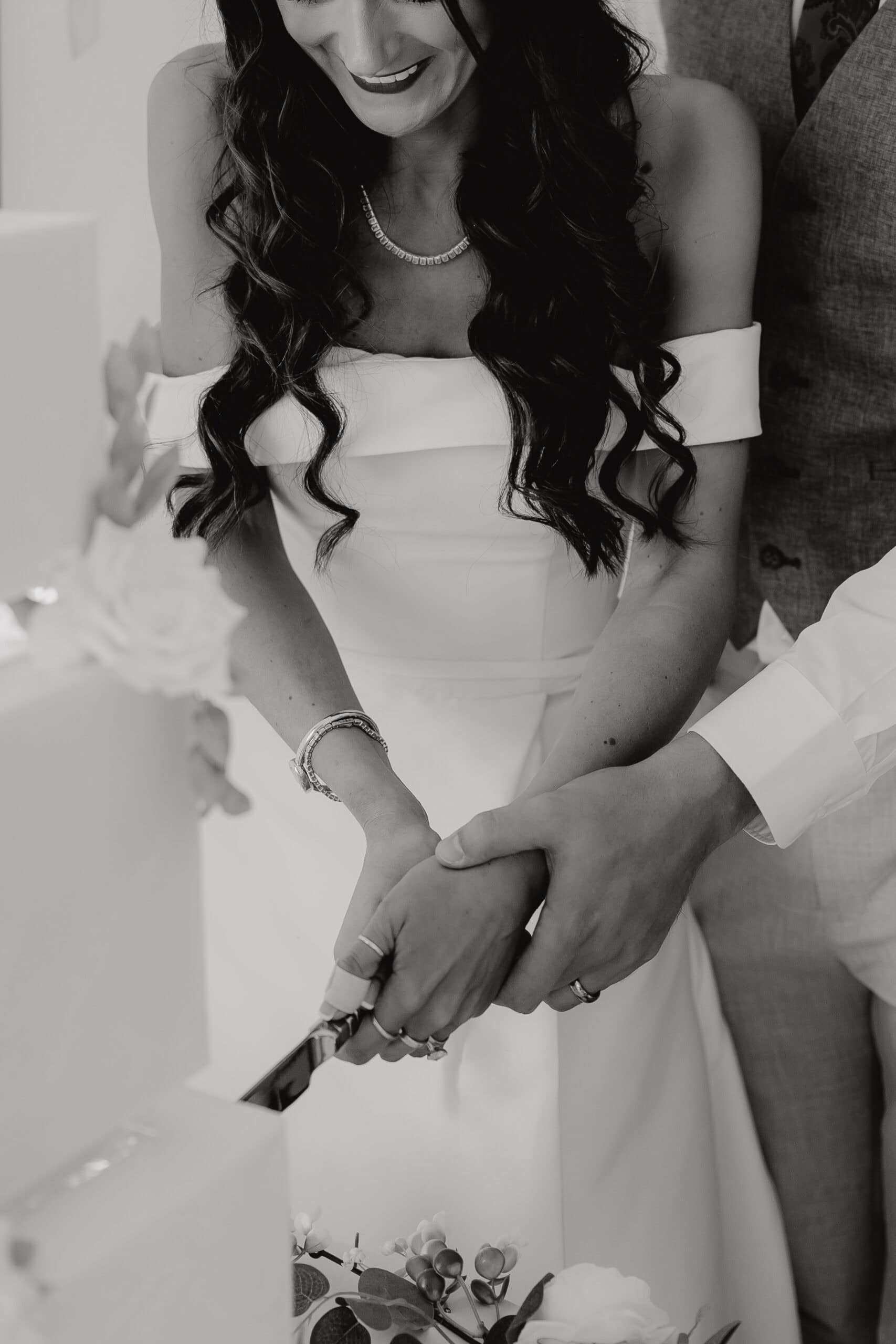 Close-up documentary wedding photography in black and white capturing the detail of a couple cutting their cake.