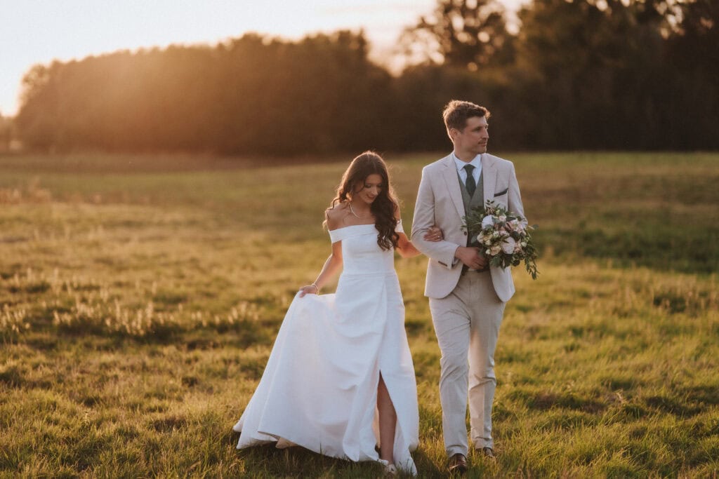 Charlotte and Harry walking through a golden field at sunset – editorial wedding photography in Essex by Tel, Lily & White