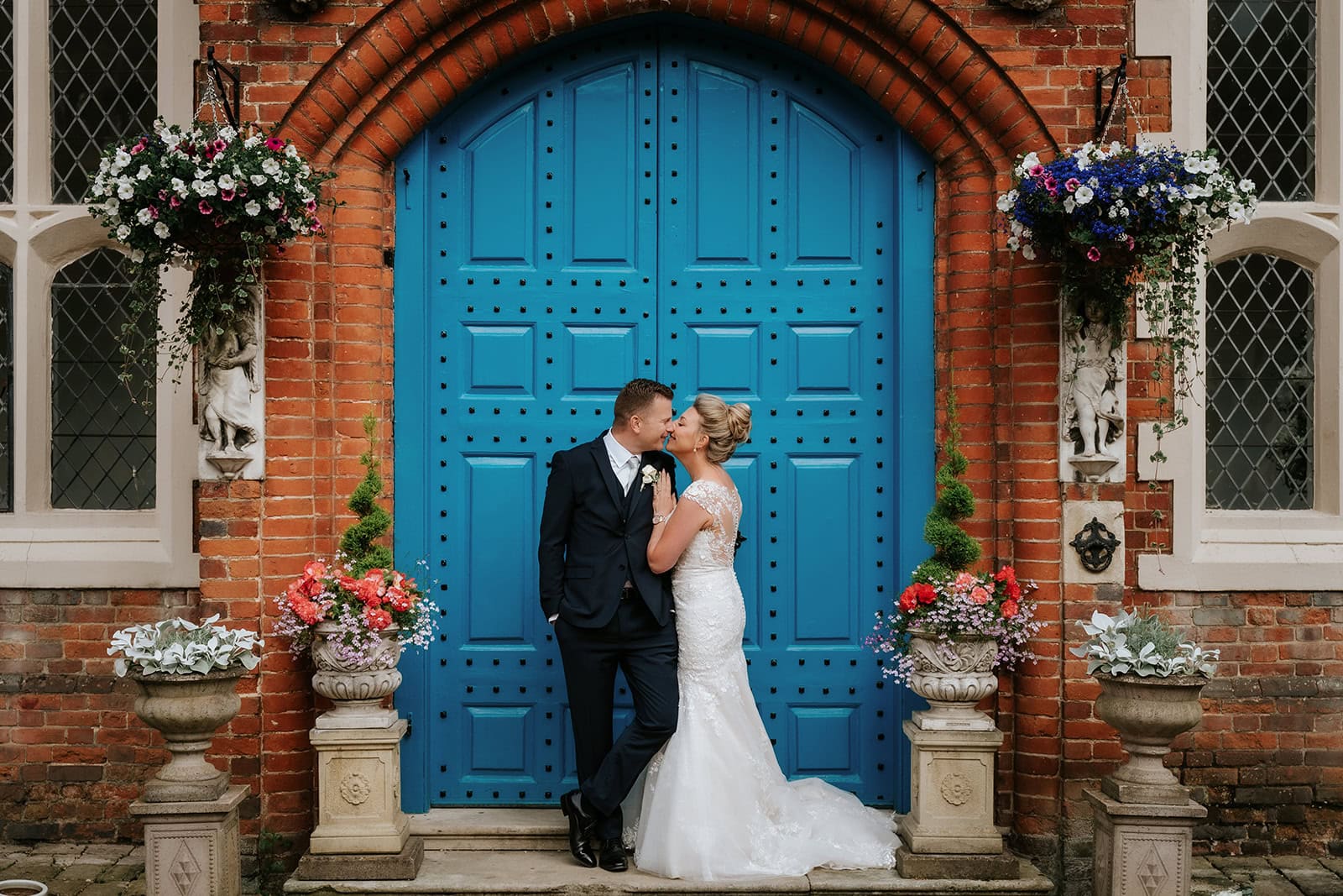 A couple sharing a tender moment outside the iconic blue doors at Gosfield Hall wedding venue in Essex