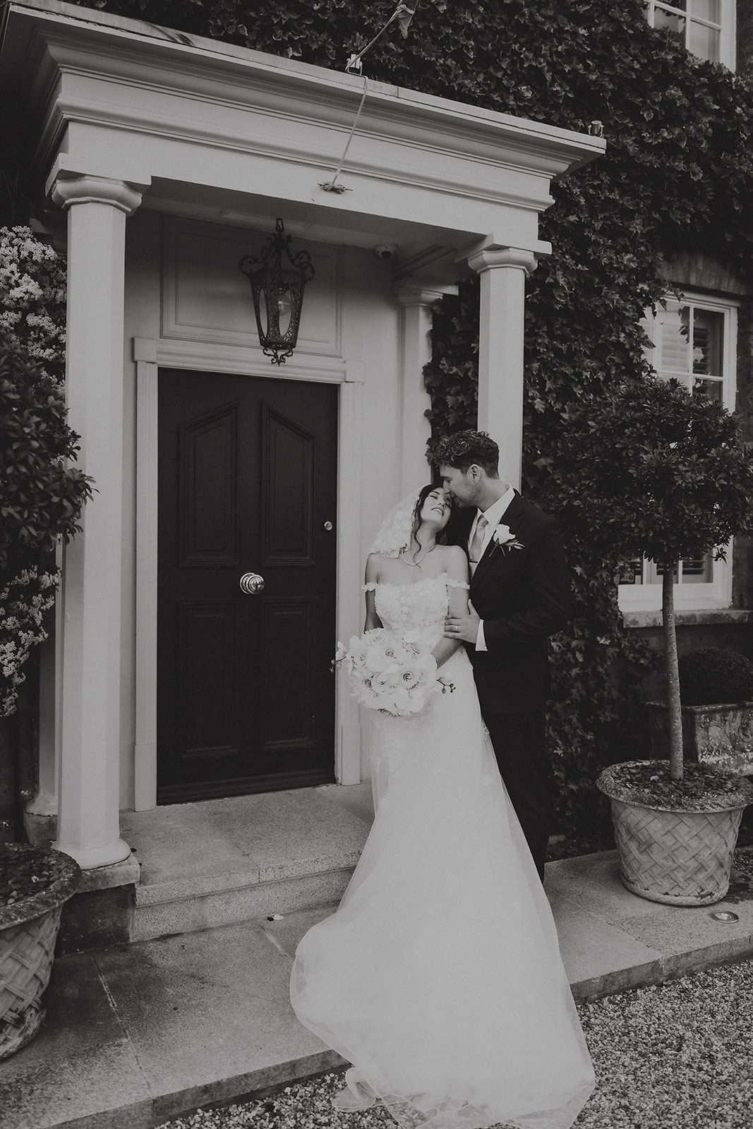 Paul and Joanna sharing an embrace in the doorway at Friern Manor, Essex on their wedding day, photographed by Tel James, Lily & White